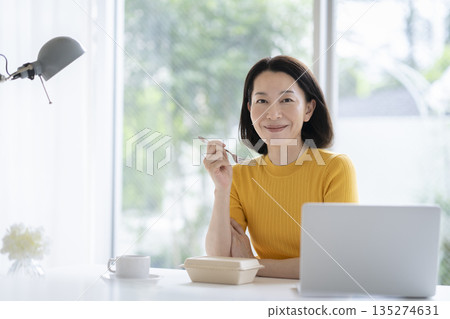 一位中年婦女在辦公桌工作間隙吃午餐的照片 135274631