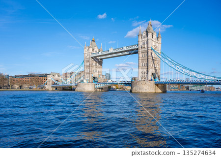 Tower Bridge stands majestically over the River Thames, showcasing its iconic structure against a clear blue sky. Visitors can admire the beauty of London from this historic landmark. 135274634