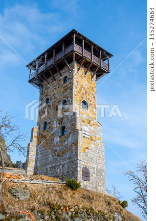The lookout tower on Wysoki Kamien in the Jizera Mountains stands tall against a blue sky. Visitors enjoy breathtaking views of the surrounding landscape and nature trails nearby. The lookout tower on Wysoki Kamien in the Jizera Mountains stands tall against a blue sky. Visitors enjoy breathtaking views of the surrounding landscape and nature trails nearby. 135274663