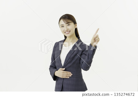 Portrait of a young Japanese woman in a suit looking at the camera and pointing at something on a white background Portrait of a young Japanese woman in a suit looking at the camera and pointing at something on a white background 135274672