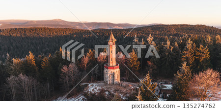 Stepanka lookout tower stands tall in the Jizera Mountains during winter. The sunset lights up the landscape, highlighting the trees and the tower. Views extend over the surrounding area. 135274762