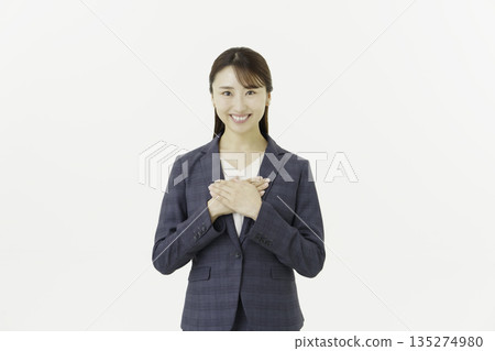 一位身穿西裝的年輕日本女性,在白色背景前,看向鏡頭,一隻手放在胸前。 一位身穿西裝的年輕日本女性,在白色背景前,看向鏡頭,一隻手放在胸前。 135274980