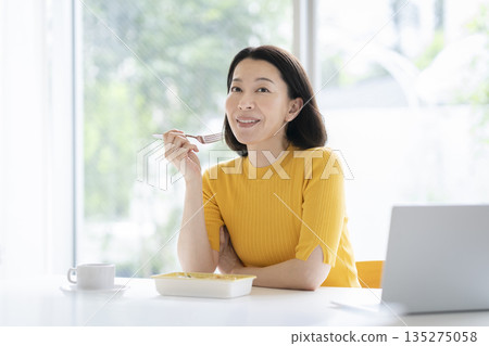 Image of a woman in her 50s eating lunch at her desk 135275058