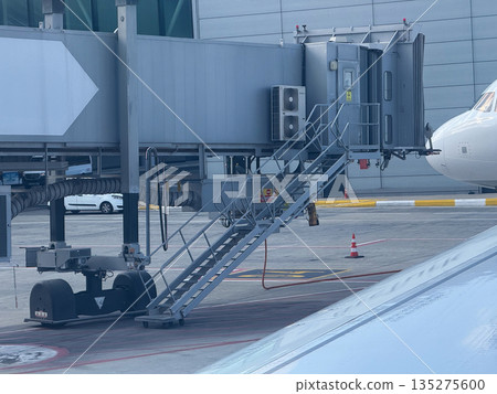 Passenger boarding bridge with stairs at airport gate. Ground infrastructure, aircraft access, and travel coordination through terminal equipment Passenger boarding bridge with stairs at airport gate. Ground infrastructure, aircraft access, and travel coordination through terminal equipment 135275600
