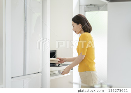 一位五十多歲的婦女正在用微波爐加熱午餐。 一位五十多歲的婦女正在用微波爐加熱午餐。 135275621
