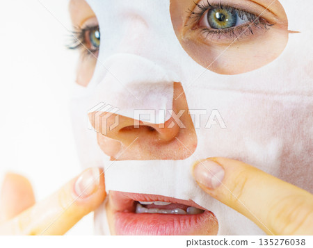 Woman applying sheet mask on face Woman applying sheet mask on face 135276038