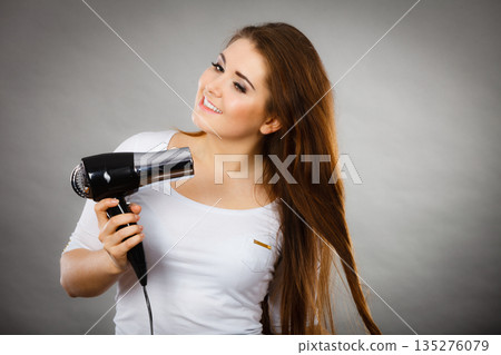 Woman drying her hair using hair dryer 135276079