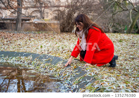 Woman walking in park in Prague during winter without snow wearing red coat. Calm urban walking, everyday lifestyle and seasonal city routine in real life European environment Woman walking in park in Prague during winter without snow wearing red coat. Calm urban walking, everyday lifestyle and seasonal city routine in real life European environment 135276380