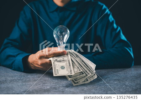 Businessman holding light bulb and dollar bills for business idea, where global marketing concept leads to growth while leadership and innovation knowledge ensure profit management 135276435
