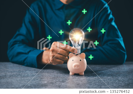 Financial innovation concept shows hand putting glowing lightbulb into piggy bank for wealth growth, representing creative business ideas and smart financial investment strategies Financial innovation concept shows hand putting glowing lightbulb into piggy bank for wealth growth, representing creative business ideas and smart financial investment strategies 135276452