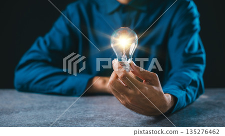 Hand holds glowing bulb light moment for idea, innovation, lightbulb, business background concept, power, digital inspiration flows through creative mind while person sits at desk 135276462