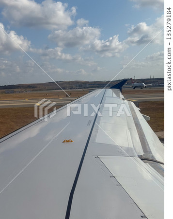 Airplane wing seen from passenger window on runway. Preflight movement, aircraft structure, and travel anticipation through aviation perspective 135279184