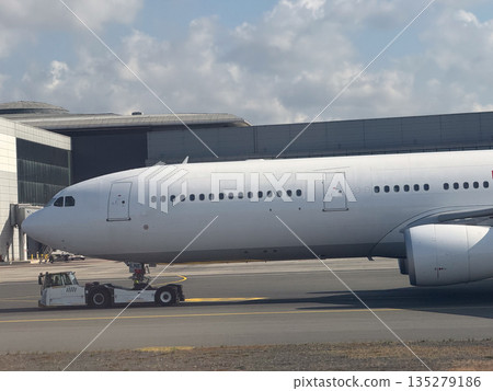 Passenger airplane nose being pushed by tow tractor. Ground maneuvering, airport logistics, and aircraft positioning through aviation support vehicles. Passenger airplane nose being pushed by tow tractor. Ground maneuvering, airport logistics, and aircraft positioning through aviation support vehicles. 135279186