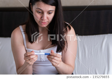 Woman Holding Positive Pregnancy Test with Worried Expression Woman Holding Positive Pregnancy Test with Worried Expression 135279855