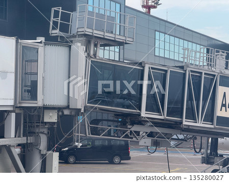 Airport jet bridge and terminal facade with service vehicle. Ground infrastructure, passenger transfer, and aviation support through technology, engineering, and logistics Airport jet bridge and terminal facade with service vehicle. Ground infrastructure, passenger transfer, and aviation support through technology, engineering, and logistics 135280027
