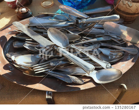 Antique flea market in Europe, Italy. Vintage items. Set of old tableware. Retro knives and spoons, background for design. Antique flea market in Europe, Italy. Vintage items. Set of old tableware. Retro knives and spoons, background for design. 135280167