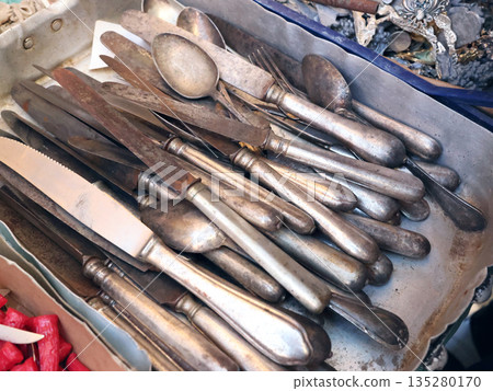 Antique flea market in Europe, Italy. Vintage items. Set of old tableware. Retro knives and spoons, background for design. 135280170