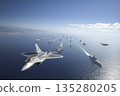 A cutting-edge fighter jet flies over an aircraft carrier strike group. 135280205