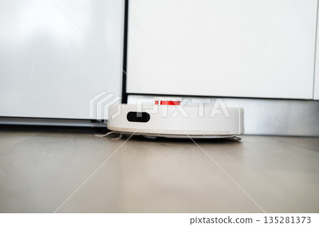 Smart robot vacuum cleaner navigating narrow space between kitchen cabinets, automated floor cleaning and modern home technology concept Smart robot vacuum cleaner navigating narrow space between kitchen cabinets, automated floor cleaning and modern home technology concept 135281373