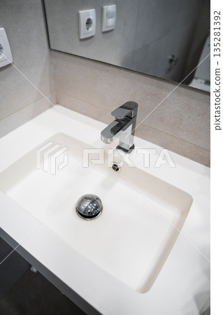 Minimalist washbasin and modern chrome tap in clean bathroom, white sink with gray tile wall and mirror, home renovation concept 135281392