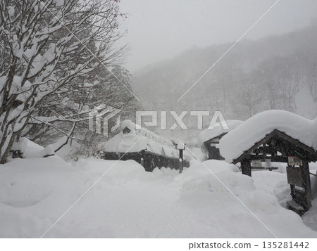 A traditional Japanese house buried in snow in a mountain village in a heavy snow region where visibility is blurred by a snowstorm 135281442