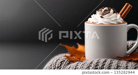 A warm mug of hot chocolate topped with whipped cream, chocolate shavings, and a cinnamon stick, placed on a cozy knitted blanket	 135282944
