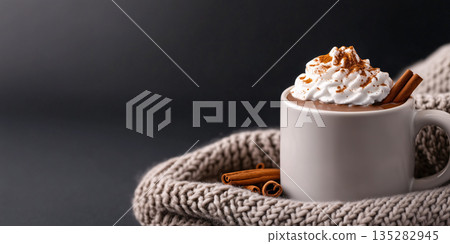 A warm mug of hot chocolate topped with whipped cream, chocolate shavings, and a cinnamon stick, placed on a cozy knitted blanket	 135282945