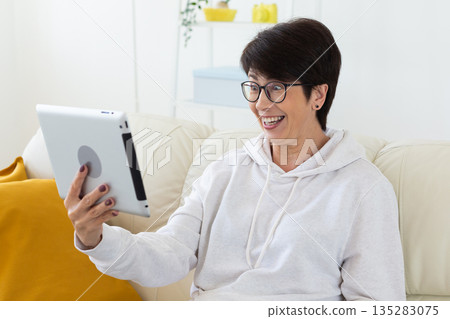 Closeup portrait of woman using tablet while sitting on sofa. Digital communication, facial expression, and emotional reaction during online conversation. 135283075