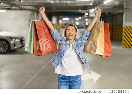 A joyful woman raises shopping bags in celebration after a successful shopping trip 135283164
