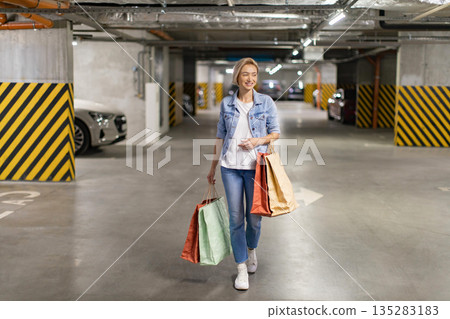A smiling woman walks through a parking garage carrying shopping bags after a successful shopping trip A smiling woman walks through a parking garage carrying shopping bags after a successful shopping trip 135283183