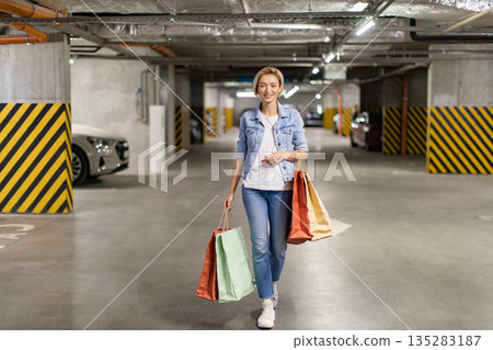 A smiling woman carries shopping bags while walking through a parking garage, ready to go home A smiling woman carries shopping bags while walking through a parking garage, ready to go home 135283187