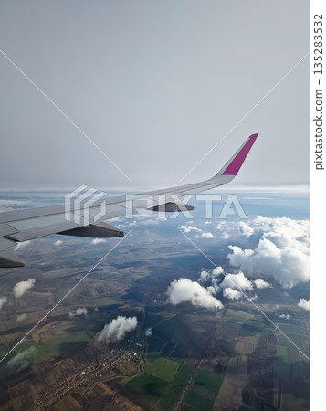 Breathtaking landing with a plane wing banking through thick, foggy clouds. View through airplane window during flight, with dynamic aerial perspective of the earth Breathtaking landing with a plane wing banking through thick, foggy clouds. View through airplane window during flight, with dynamic aerial perspective of the earth 135283532