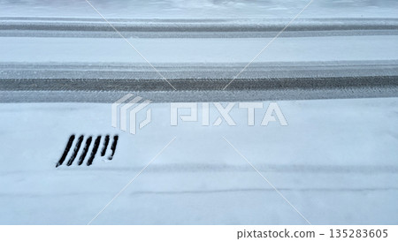Tire Tracks and Sewer Grate in Snow 135283605