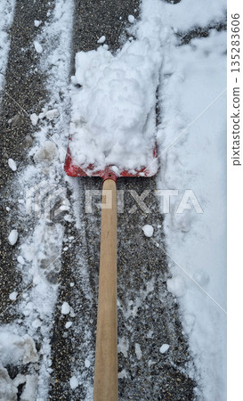 Red snow shovel with wood handle clearing driveway from fresh winter snow 135283606