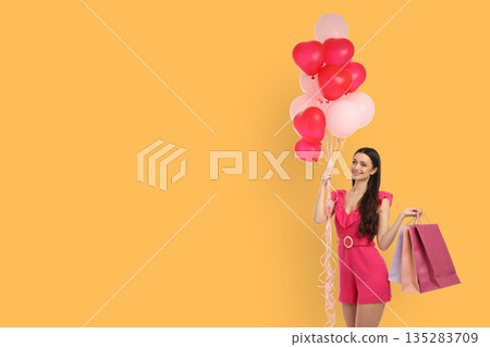 Woman in pink outfit holds heart balloons and shopping bags 135283709