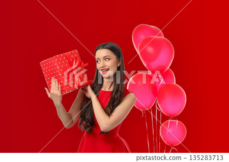Woman presents a gift box while surrounded by pink balloons Woman presents a gift box while surrounded by pink balloons 135283713