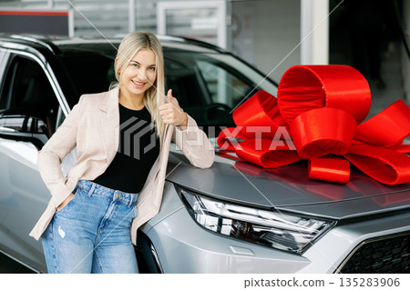 Happy businesswoman showing thumbs up near new car with red bow in dealership 135283906