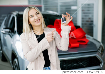 Happy business woman showing car key in dealership Happy business woman showing car key in dealership 135283916