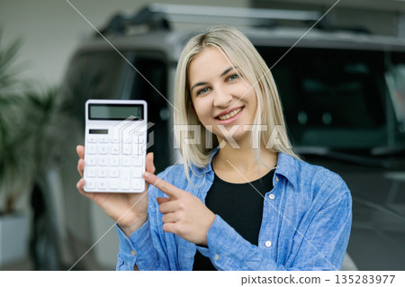 Saleswoman showing calculator and explaining car cost in dealership 135283977