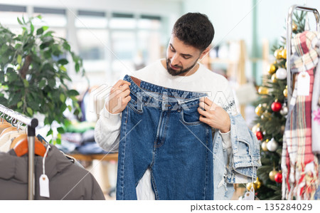 Young man choosing jeans pantaloons in clothing store during Christmas Young man choosing jeans pantaloons in clothing store during Christmas 135284029