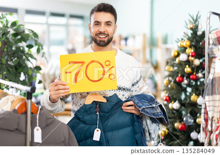 Happy young man presenting sale in clothing store at Christmas Happy young man presenting sale in clothing store at Christmas 135284049