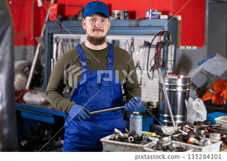 Positive male worker of car workshop holding metal tool in car workshop 135284101