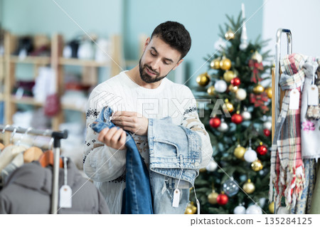 Man chooses jeans against the background of a Christmas tree in a store decorated for the holidays Man chooses jeans against the background of a Christmas tree in a store decorated for the holidays 135284125