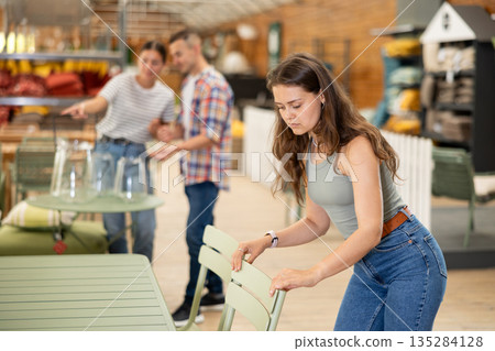 Girl thoughtfully choosing practical patio chairs in garden store Girl thoughtfully choosing practical patio chairs in garden store 135284128