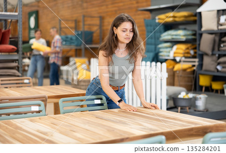 Interested girl choosing comfortable garden table in store Interested girl choosing comfortable garden table in store 135284201