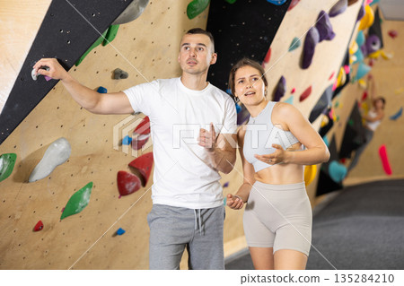 Girl gym coach and teen client standing in fitness room discussing possible options climbing 135284210