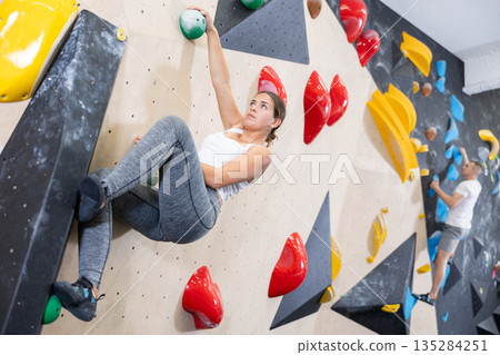 Young woman climbs steep artificial wall in sports complex and trains endurance 135284251