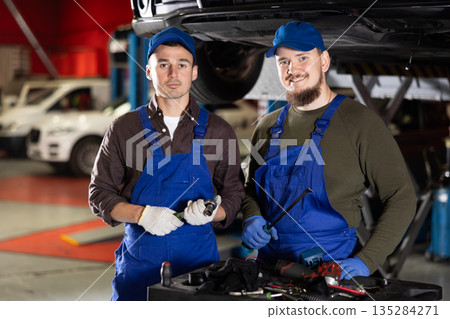 Two positive car mechanics standing in auto workshop holding repair tools Two positive car mechanics standing in auto workshop holding repair tools 135284271
