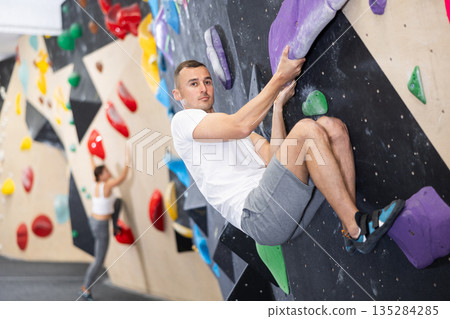 Man maneuvering on artificial bouldering wall in climbing center 135284285