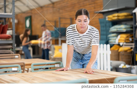 Girl buyer choose table desk in garden furniture store showroom Girl buyer choose table desk in garden furniture store showroom 135284308